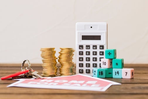 Calculatrice, piles de pièces et cubes de calcul posés sur une table, pour évoquer le coût d'un abonnement