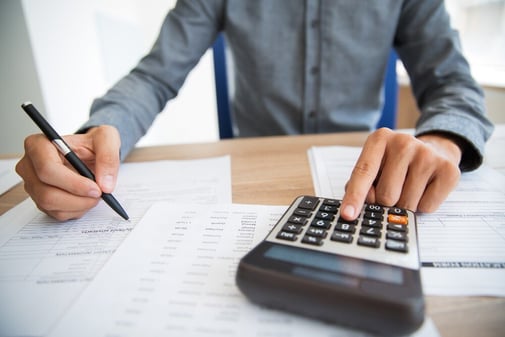 Une personne annote des documents financiers d'un stylo et saisit des montants sur une calculatrice