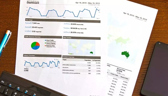 Rapports imprimés de statistiques web avec courbes et camembert, posés près d'un clavier, d'un stylo et d'un smartphone