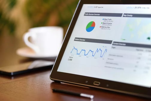 Tablette affichant un tableau de bord de statistiques avec camembert et courbe de visiteurs, à côté d'une tasse