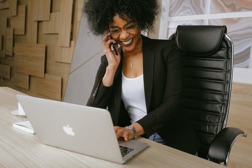 Une femme souriante au téléphone tape sur son ordinateur portable à son bureau