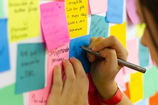 Une main écrit sur un mur de post-it colorés pour planifier les étapes d'un projet