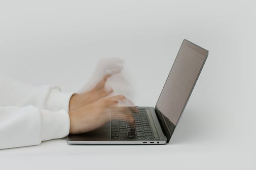 Des mains floues de vitesse tapent sur le clavier d'un ordinateur portable posé sur une table blanche