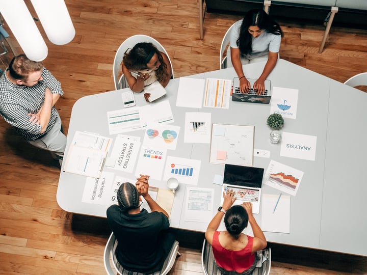 Vue du dessus d'une équipe autour d'une table couverte de documents de stratégie marketing, de graphiques et d'ordinateurs
