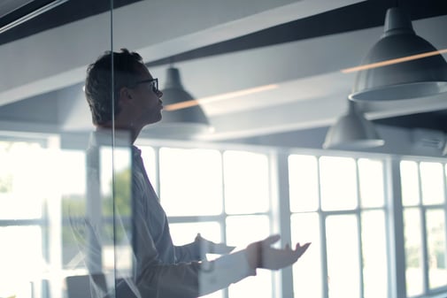 Consultant à lunettes présentant un projet en réunion derrière une paroi vitrée, dans un bureau lumineux