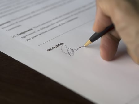 Main signant un contrat au stylo sur la ligne « Signature » d'un document papier